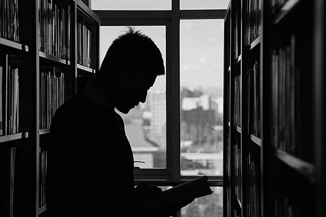 Muž v knižnici pozerajúci sa do knihy