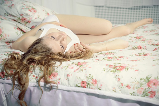 Žena s dlhými vlasmi, v bielom tielku s výstrihom leží blažene na posteli.jpg