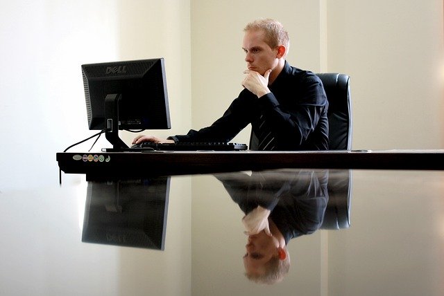 Zamyslený muž v čiernej košeli sedí pri stole a pozerá do počítača